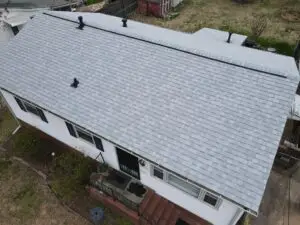 Aerial view showing a newly installed light gray asphalt shingle roof on a single-story white house.