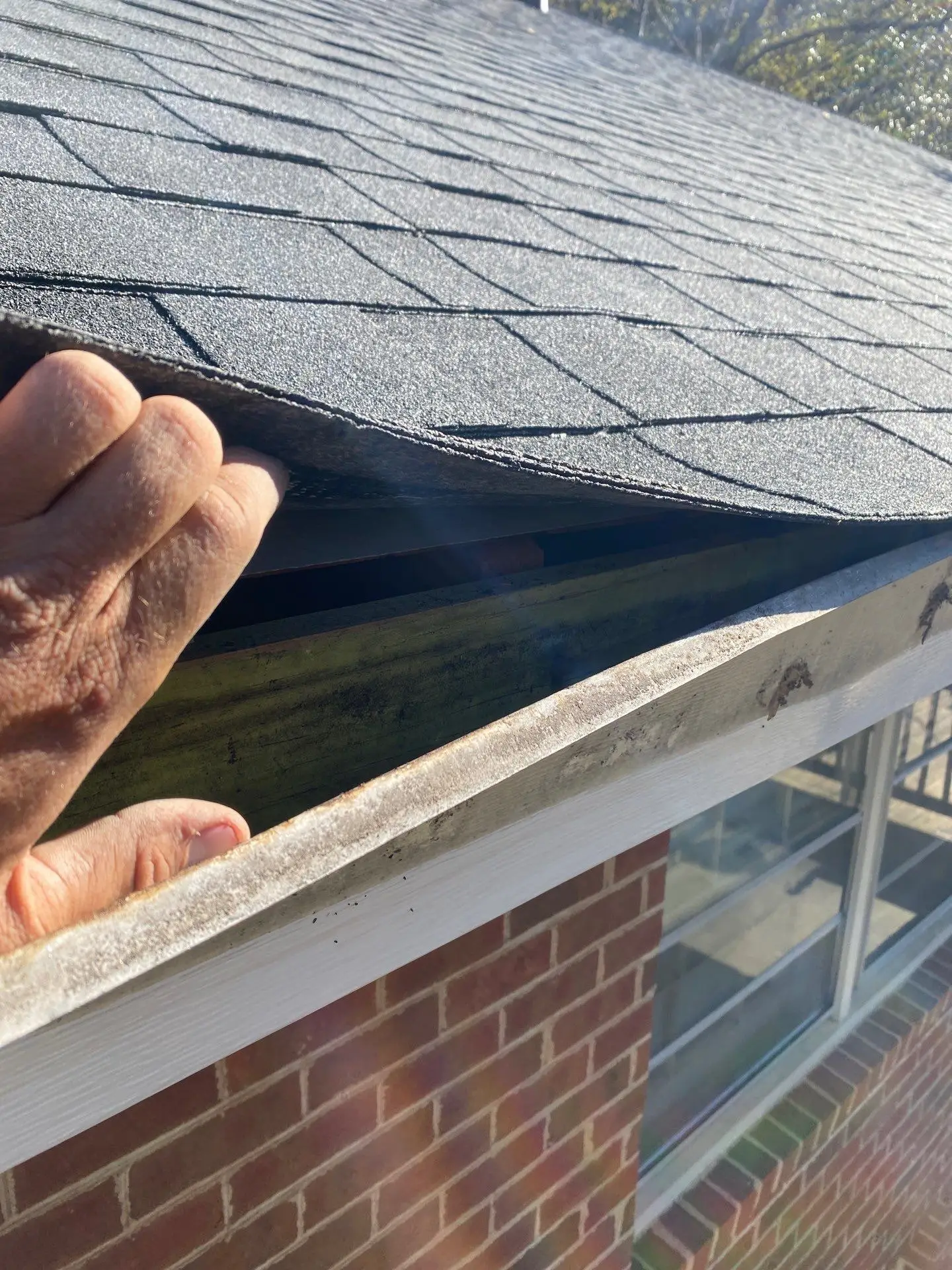 Close-up of a hand lifting the roof edge to inspect the gutters and drip edge