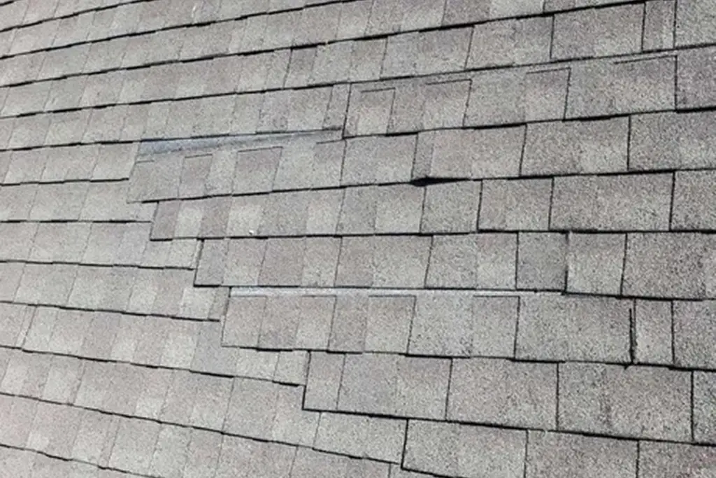 Close-up of worn asphalt shingles on a residential roof with visible uneven areas and aging.
