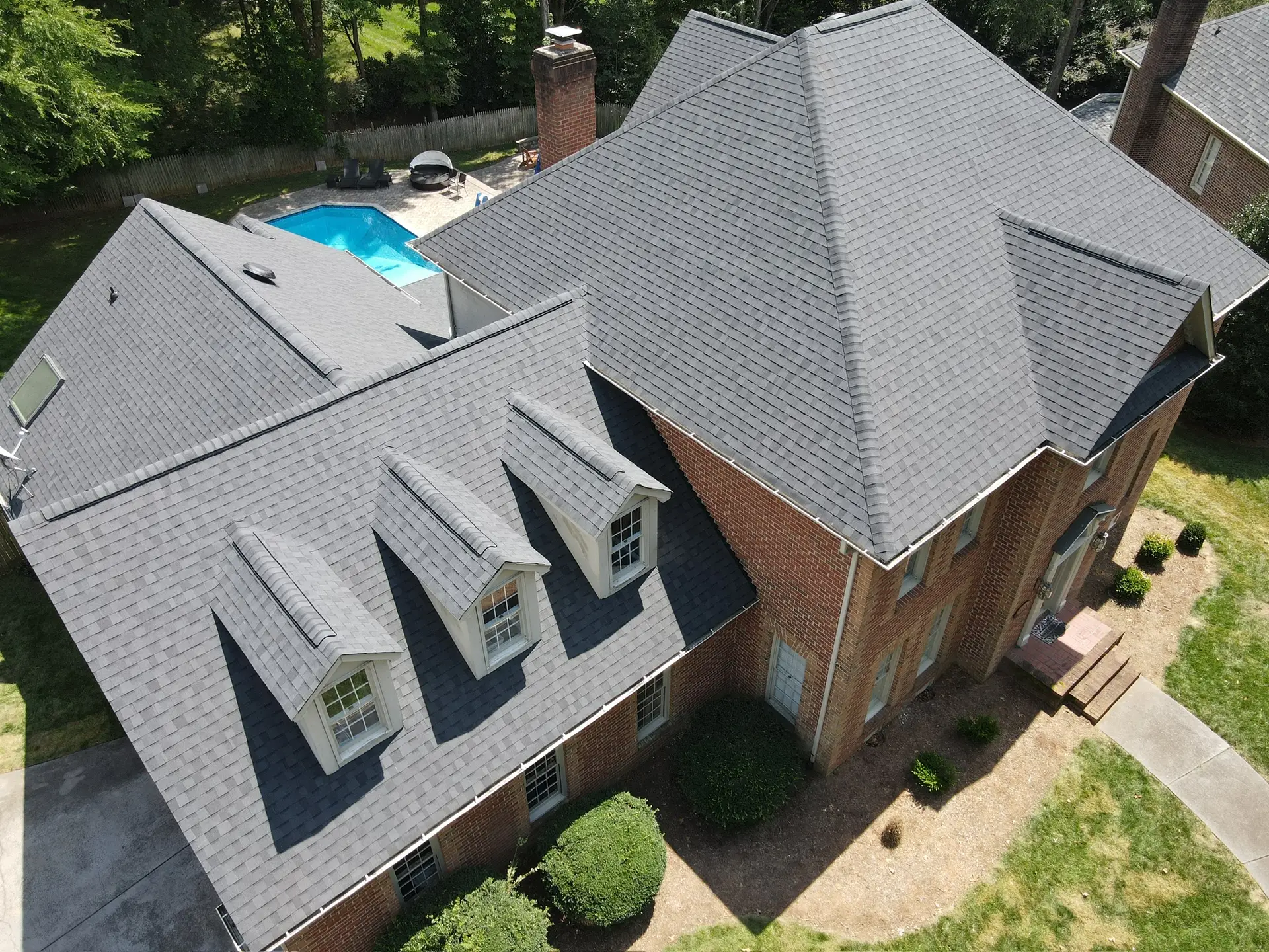 Gray shingle roof with three matching dormer windows on a brick home