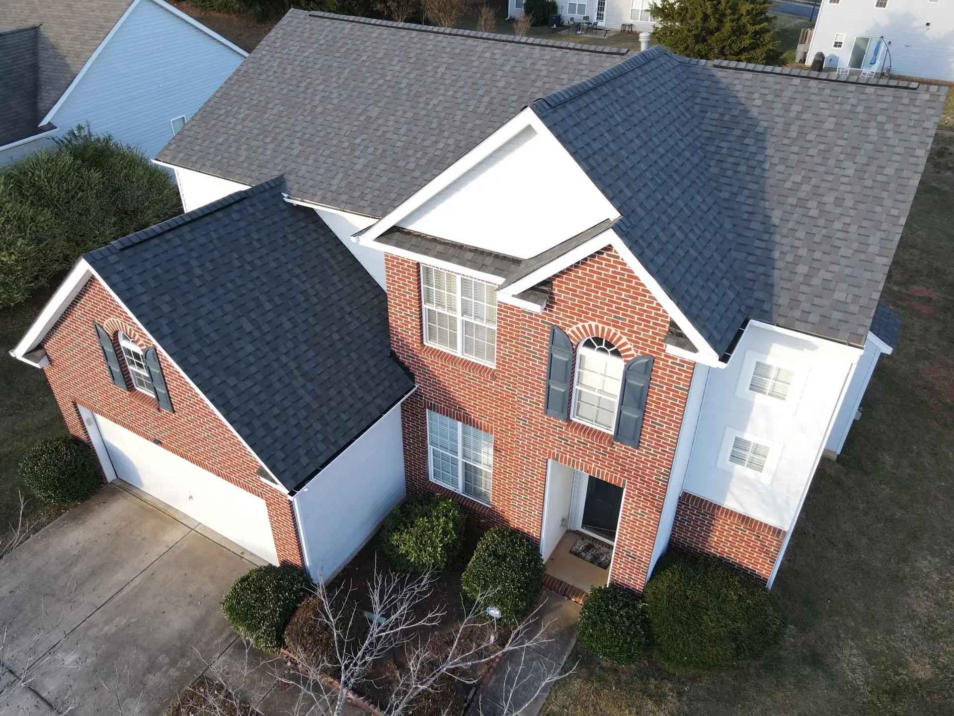 Aerial photo showing a red brick home with white siding, featuring a newly installed dark gray asphalt shingle gable roof.