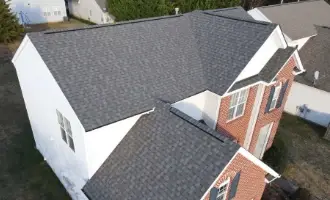 A two-story home with red brick and white siding featuring a new dark gray asphalt shingle gable roof.