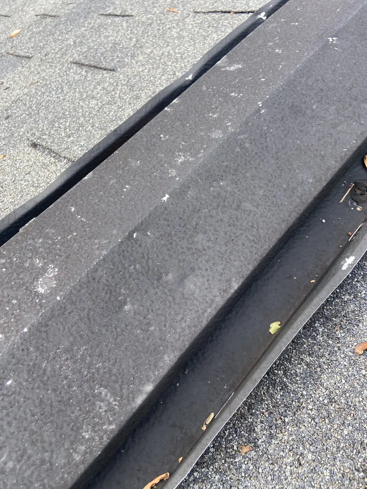 Black rolled roofing on a low-slope roof edge next to the gutter