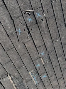 Chalk-marked hail hits on asphalt shingles during a storm damage inspection
