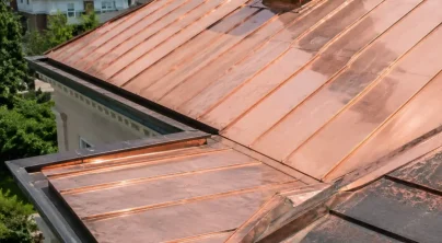 Close-up of a finished standing seam copper roof with a valley and gutter, showing the bright reddish-orange tone of newly installed copper panels