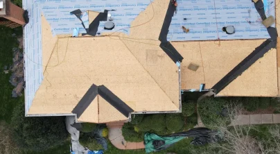 Aerial view of a roof deck under construction, with plywood sheathing exposed and ice-and-water shield and synthetic underlayment being installed ahead of roof installation