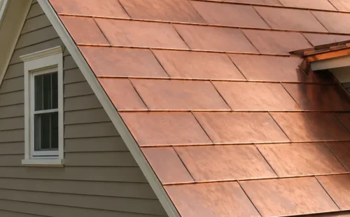Close-up of a steep copper shingle roof with staggered rectangular panels, next to a window and gray siding